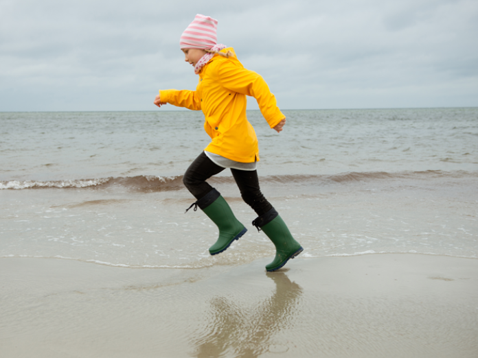 Pige løber på strand i regnvejr